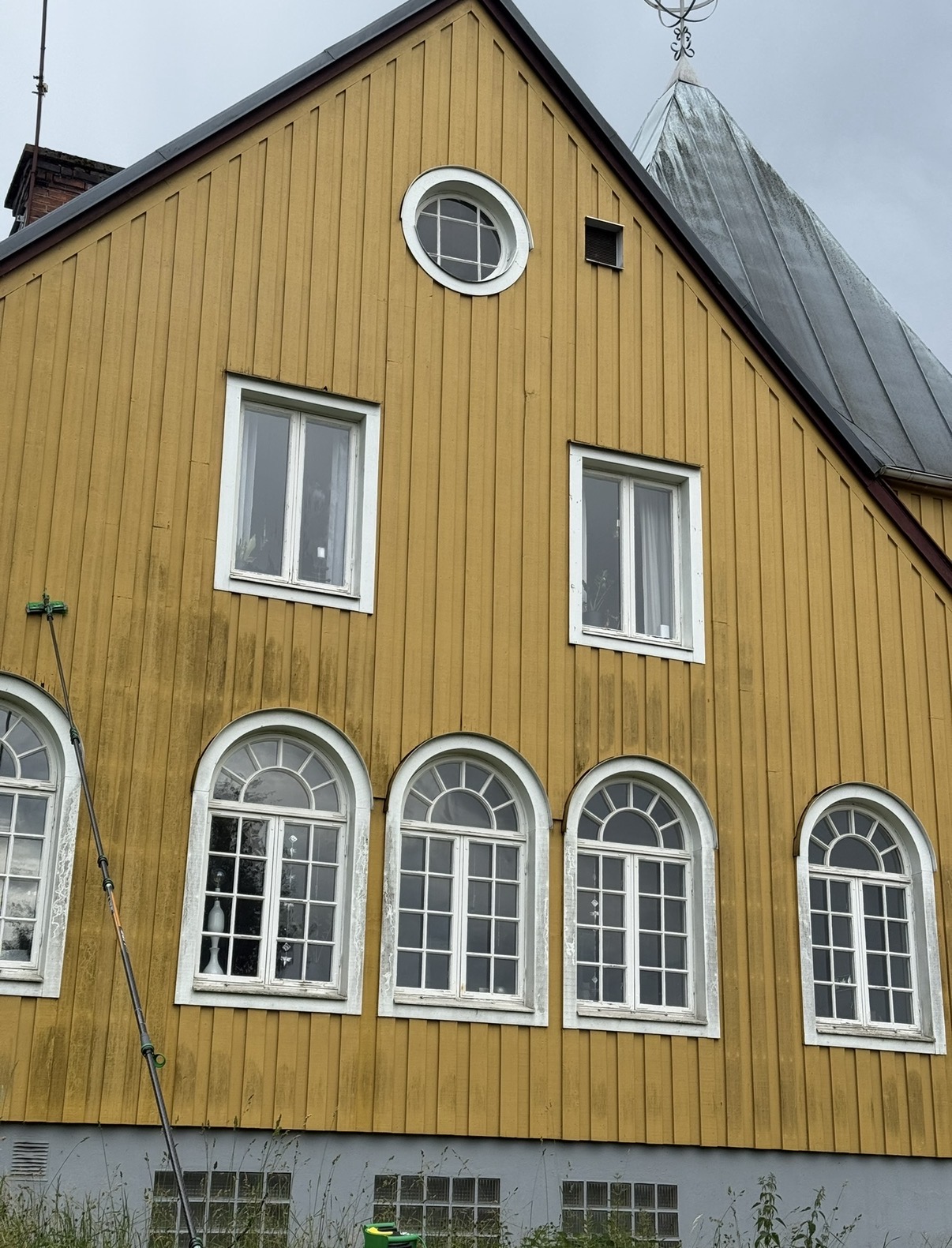 Fasadtvätt pågår med teleskopstång och borste mot gul träpanel
